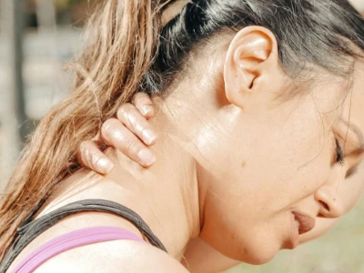 Mulher segurando a região do pescoço com expressão de dor, mostrando desconforto que pode ser aliviado com alongamentos e cuidados adequados.