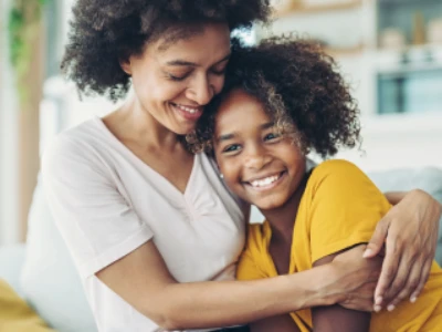 Mãe e filha juntas e sorrindo sentadas no sofá