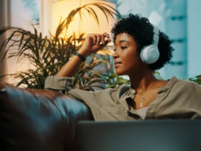 Mulher sentada em sala de estar aconchegante, com fones de ouvido, parece relaxar.