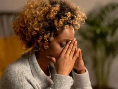 Mulher sentindo os sintomas de uma dor de cabeça intensa ou enxaqueca, cobrindo os rosto com as mãos para aliviar a pressão.