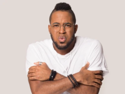 Homem com óculos e camiseta branca está abraçando a si mesmo, com um semblante de quem sente frio.