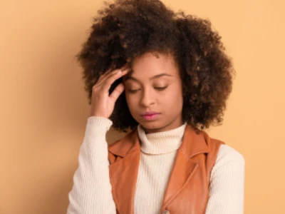 Mulher olhando para baixo, tocando a testa com os dedos da mão direita. O pano de fundo combina com sua roupa.