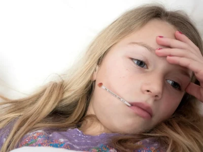 Criança com termômetro oral, expressão de desconforto, simbolizando febre infantil e a necessidade de antitérmicos Nome: menina-com-febre