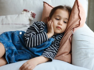 Menina deitada de lado no sofá, com a mão no rosto e expressão cansada.