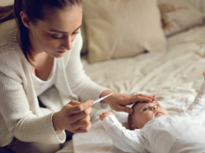 Mãe aferindo a febre do seu bebê, que está deitado na cama.