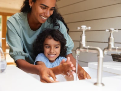 Mulher e criança parecem se divertir enquanto lavam as mãos juntos na pia