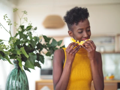 Mulher, vestindo uma blusa amarela, come uma laranja.