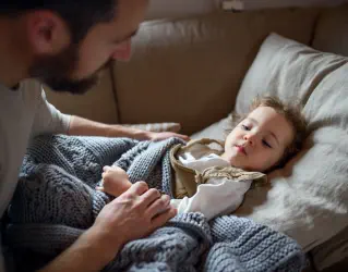 Adulto checando criança doente deitada no sofá com uma coberta