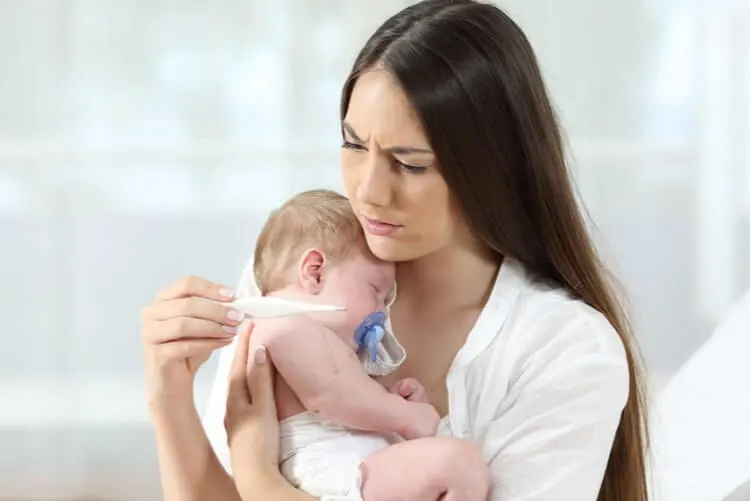 Mulher com expressão de preocupada, olhando para o termômetro em sua mão direita e segurando um bebe de colo com a mãe esquerda