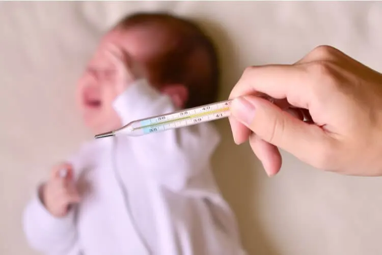 Mão segurando um termômetro com um bebê ao fundo chorando
