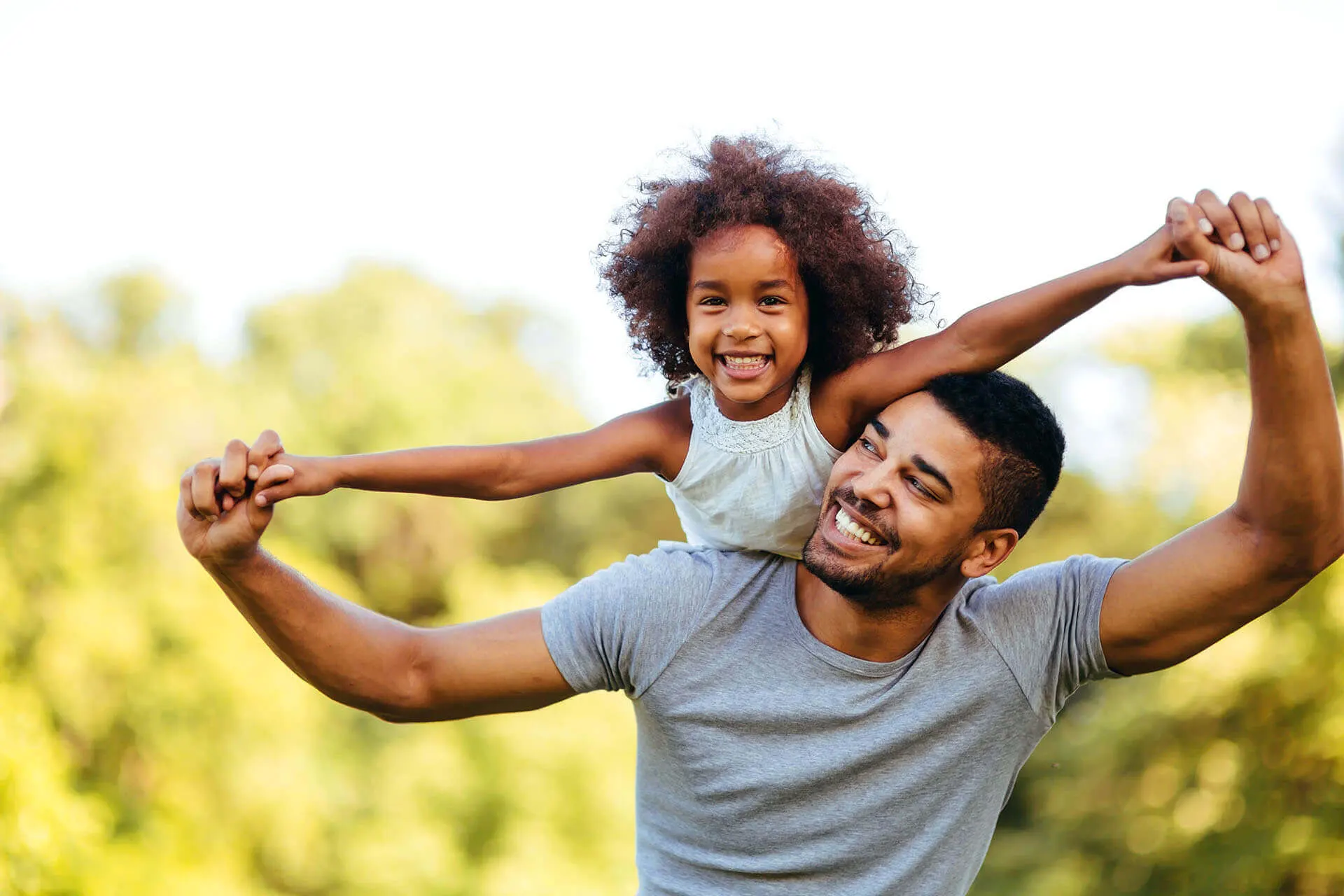 Homem negro sorrindo enquanto levanta sua filha nos braços
