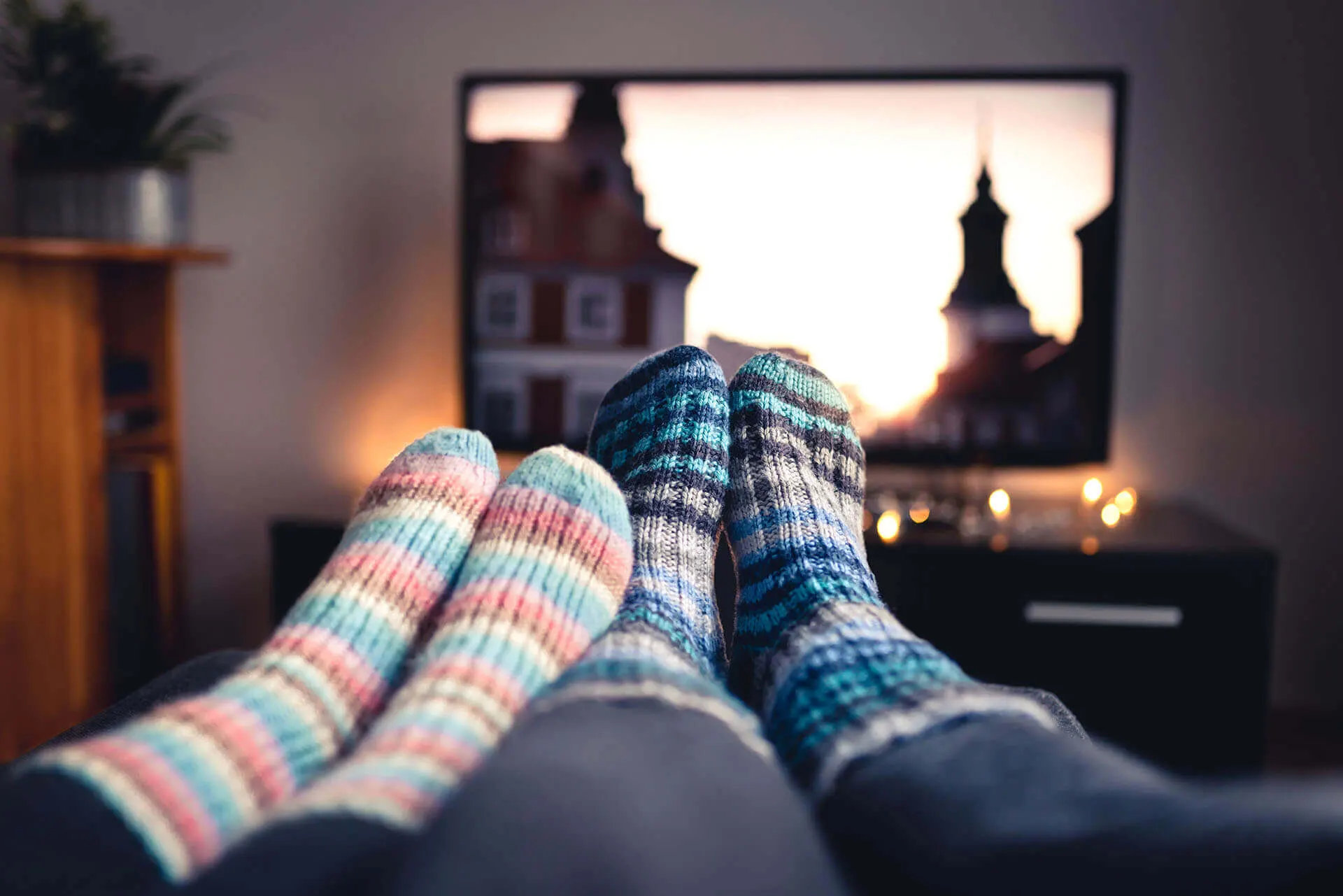 Dois pares de pés usando meias de lã em frente a uma televisão