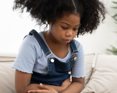 Menina que parece triste está sentada, com os braços cruzados na região da barriga.