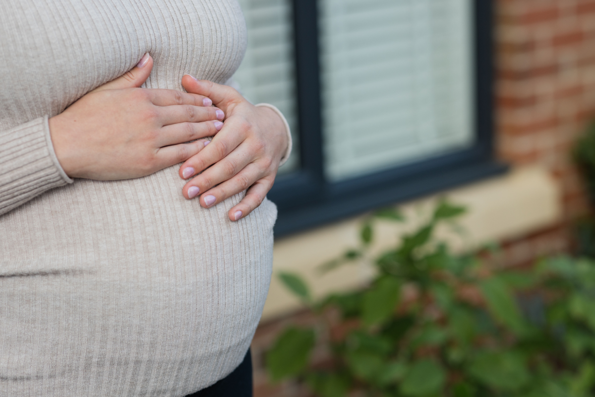 Detalhe da barriga de uma mulher grávida. Ela está com as mãos sobre a barriga, carinhosamente, na região do estômago.