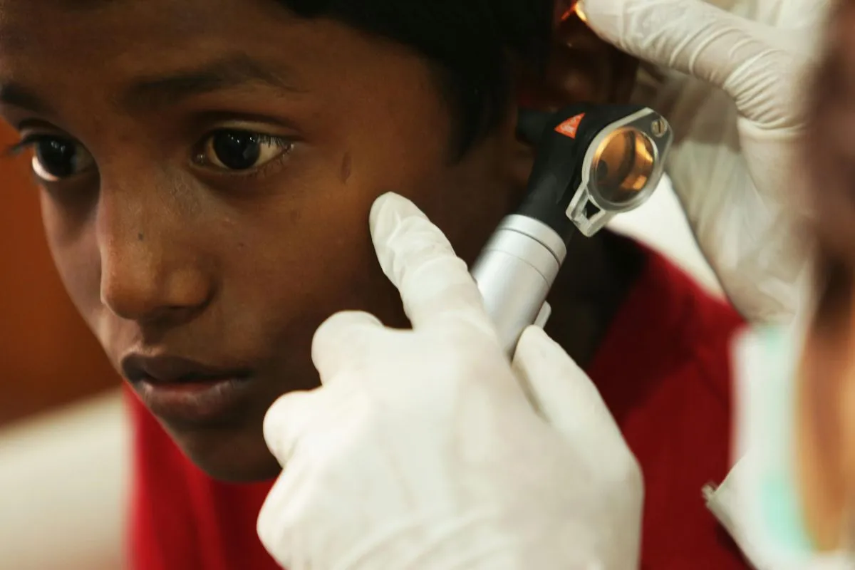 Close-up de um médico com luvas usando um otoscópio para examinar o ouvido de uma criança.