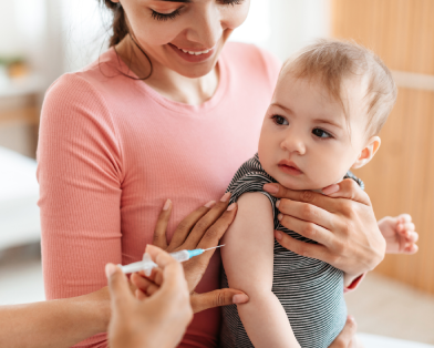 Mãe segurando bebê que está para ser vacinado. Na cena, vemos a agulha.
