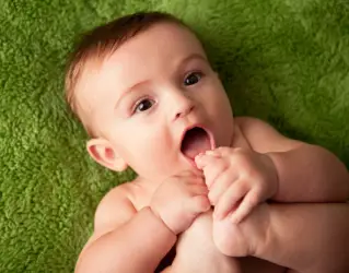 Bebê pequeno e feliz levando o pezinho à boca