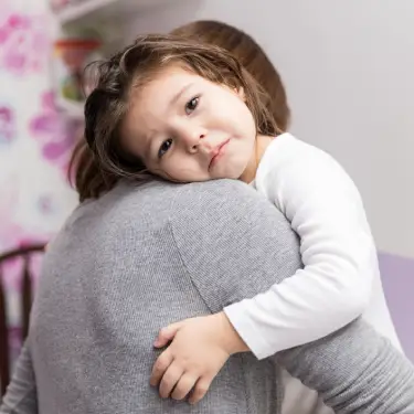 Criança no colo da mãe, com olhar cansado e choroso.