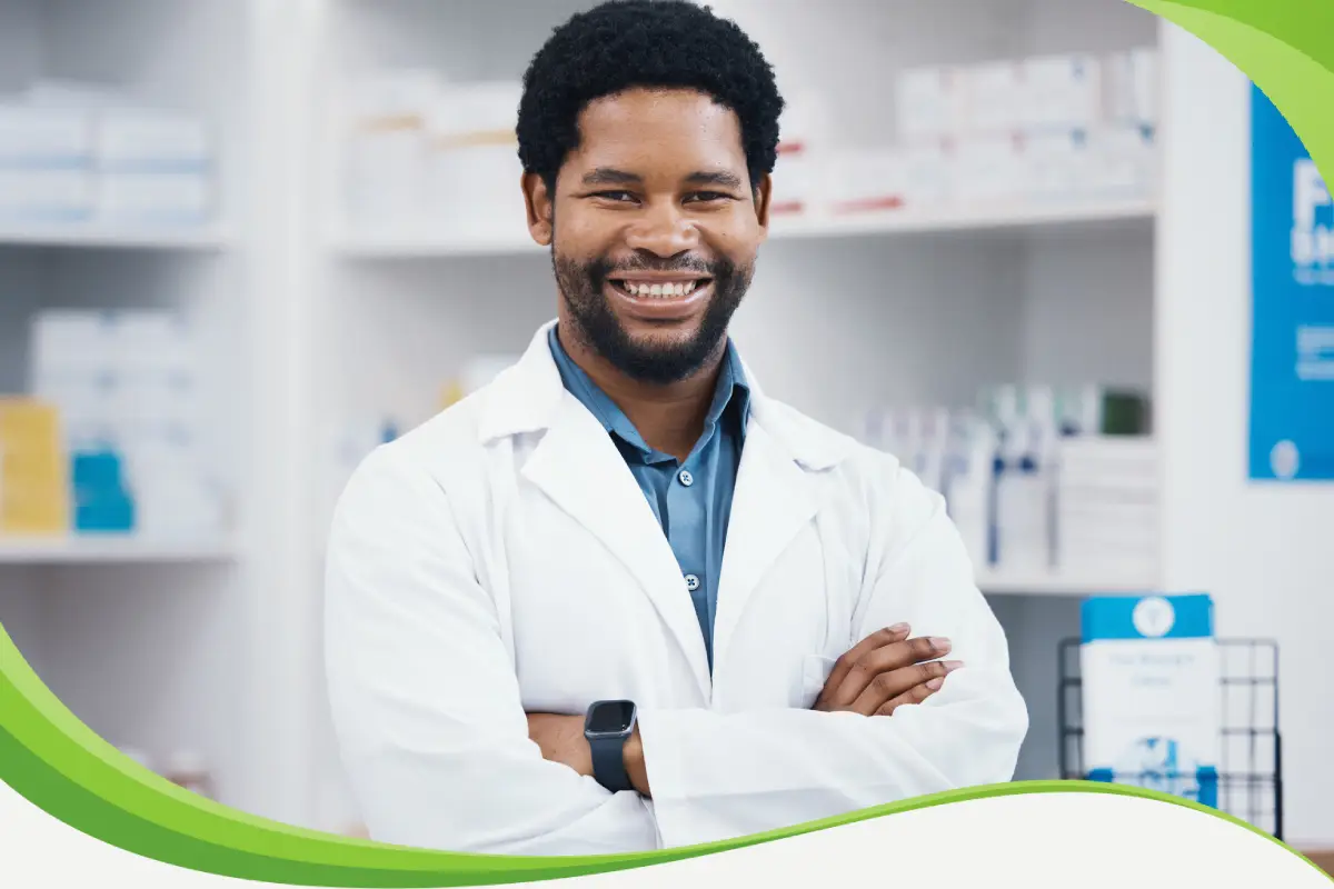 Farmacêutico em drogaria, de braços cruzados, sorrindo fazendo pose profissional para a foto.