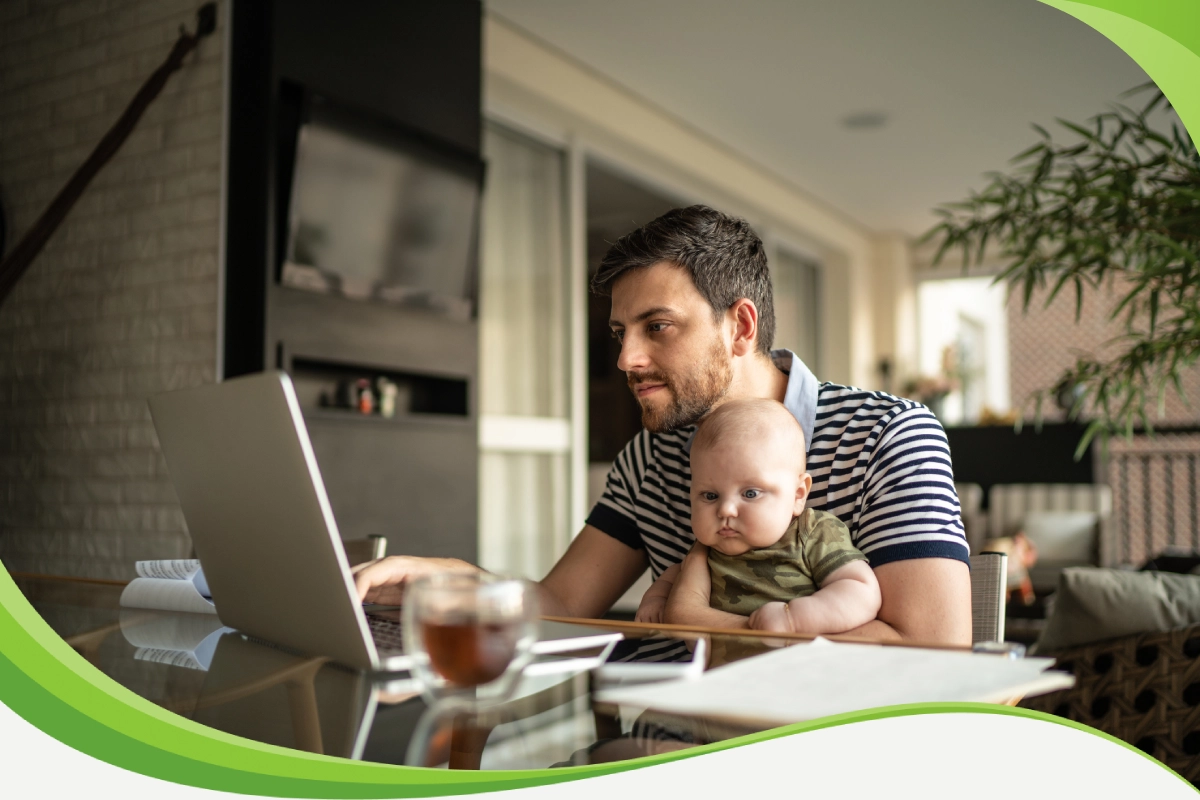 Homem segura seu bebê no colo enquanto procura informações em seu computador.