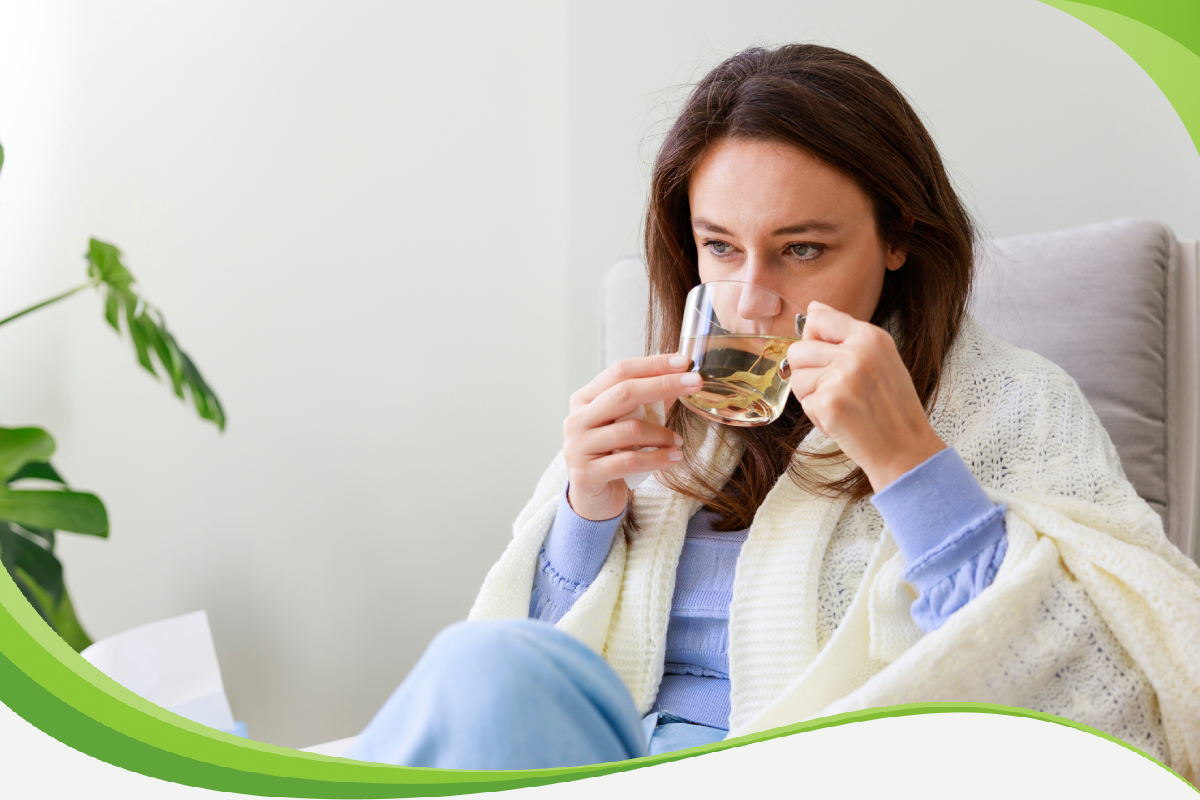 Mulher agasalhada sentada em poltrona tomando chá