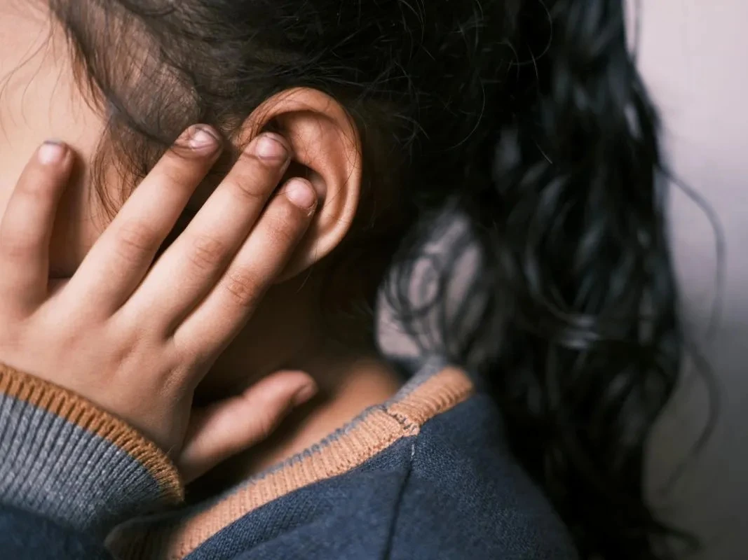 Close-up de uma criança com a mão na orelha, demonstrando o sintoma de dor de ouvido.