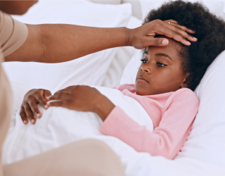 Mãe está medindo a temperatura da febre de sua filha com a mão. A criança está deitada, coberta.