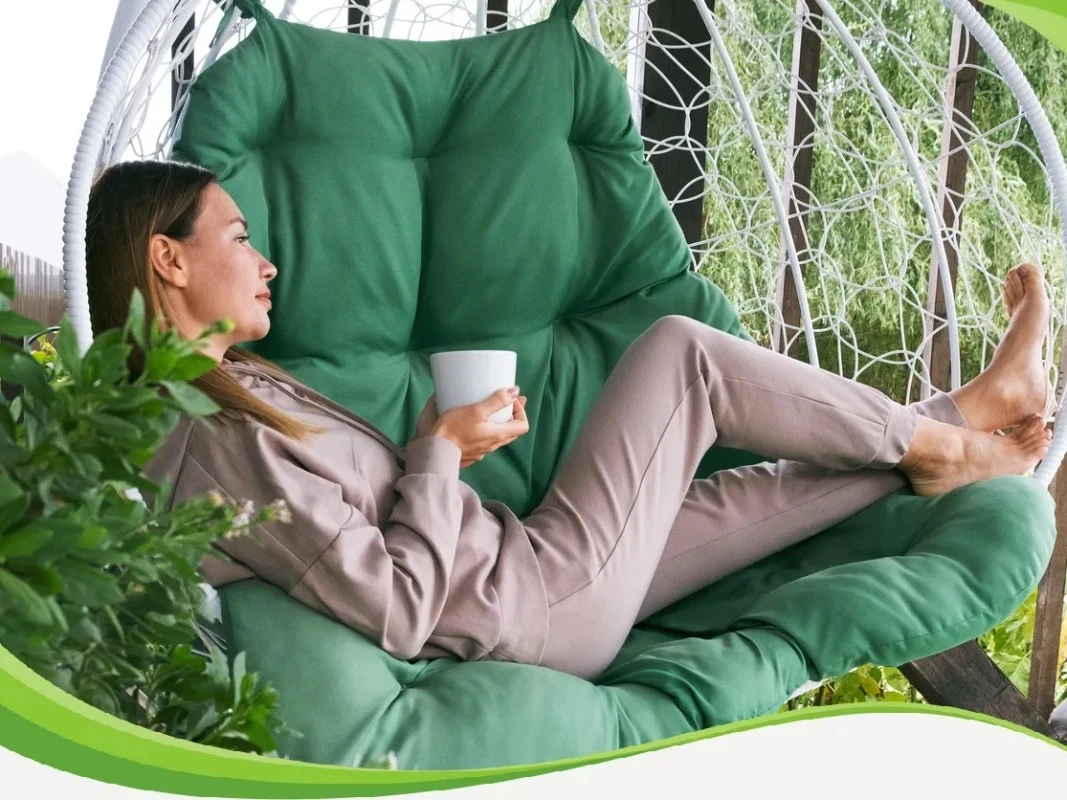 Mulher relaxada sentada em uma cadeira de balanço suspensa ao ar livre, segurando uma xícara branca e aproveitando um momento de repouso necessário para a recuperação de gripe ou resfriado.