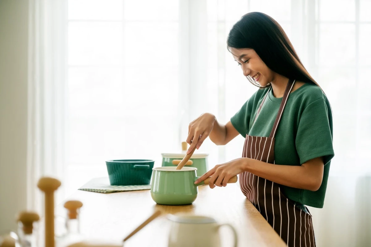 Mulher de avental na cozinha mexendo uma panela no fogão, preparando uma refeição nutritiva para ajudar a fortalecer o sistema imunológico contra vírus da gripe.